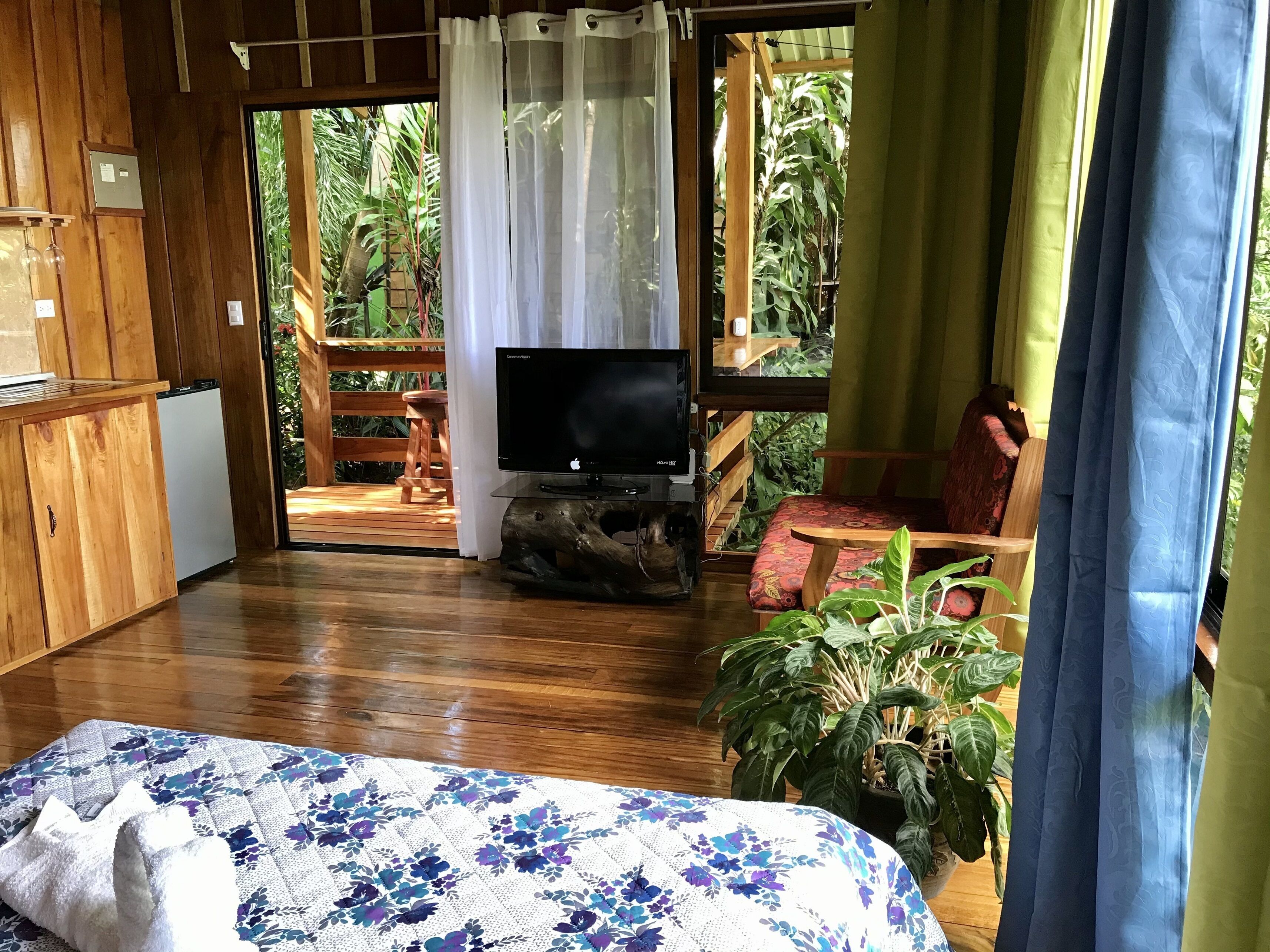 A room with a bed, a television on a wooden stand, a small refrigerator, and a wooden desk.