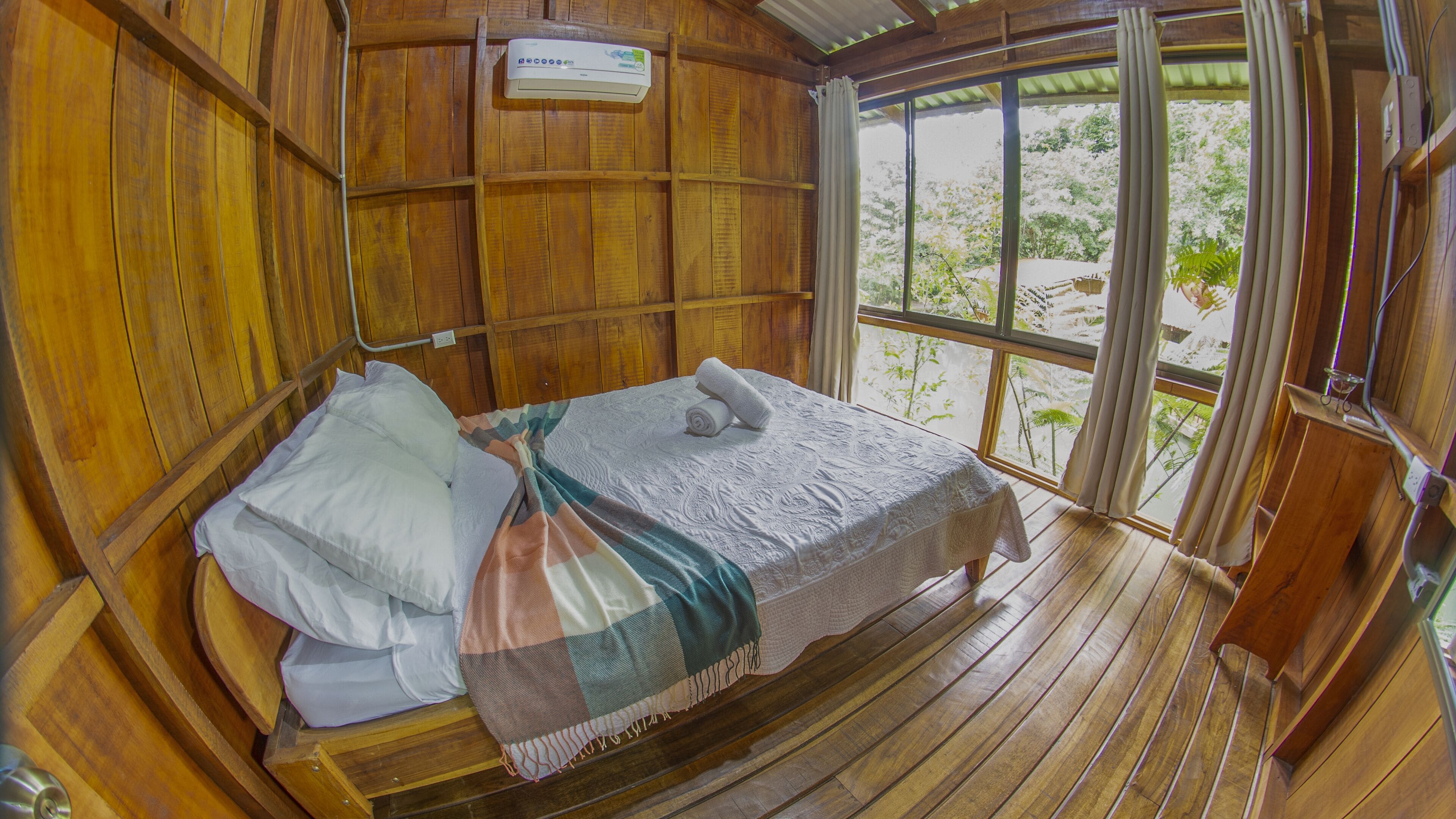 A wooden room with a bed, a window, and a ceiling fan.