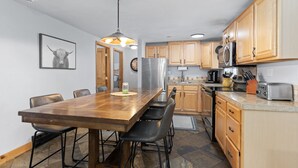 A kitchen with wooden cabinets, a stainless steel refrigerator, a microwave, and a toaster. There is a dining table with chairs and a pendant light above it.