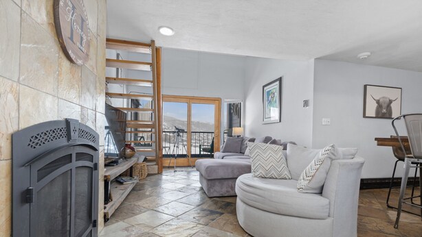 A living room with a fireplace, a sofa, a dining area, and a view of the mountains.