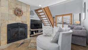 A living room with a fireplace, a television, a sofa, and a balcony with a wooden railing.