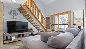 A living room with a wooden staircase, a flat-screen TV, a sofa, and a large window with a view of a snowy landscape.