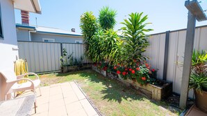 Un patio trasero con terraza, cerca de madera y varias plantas.