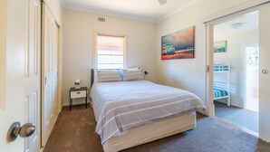 Un dormitorio con cama, mesita de noche, ventana y puerta que da a un balcón.