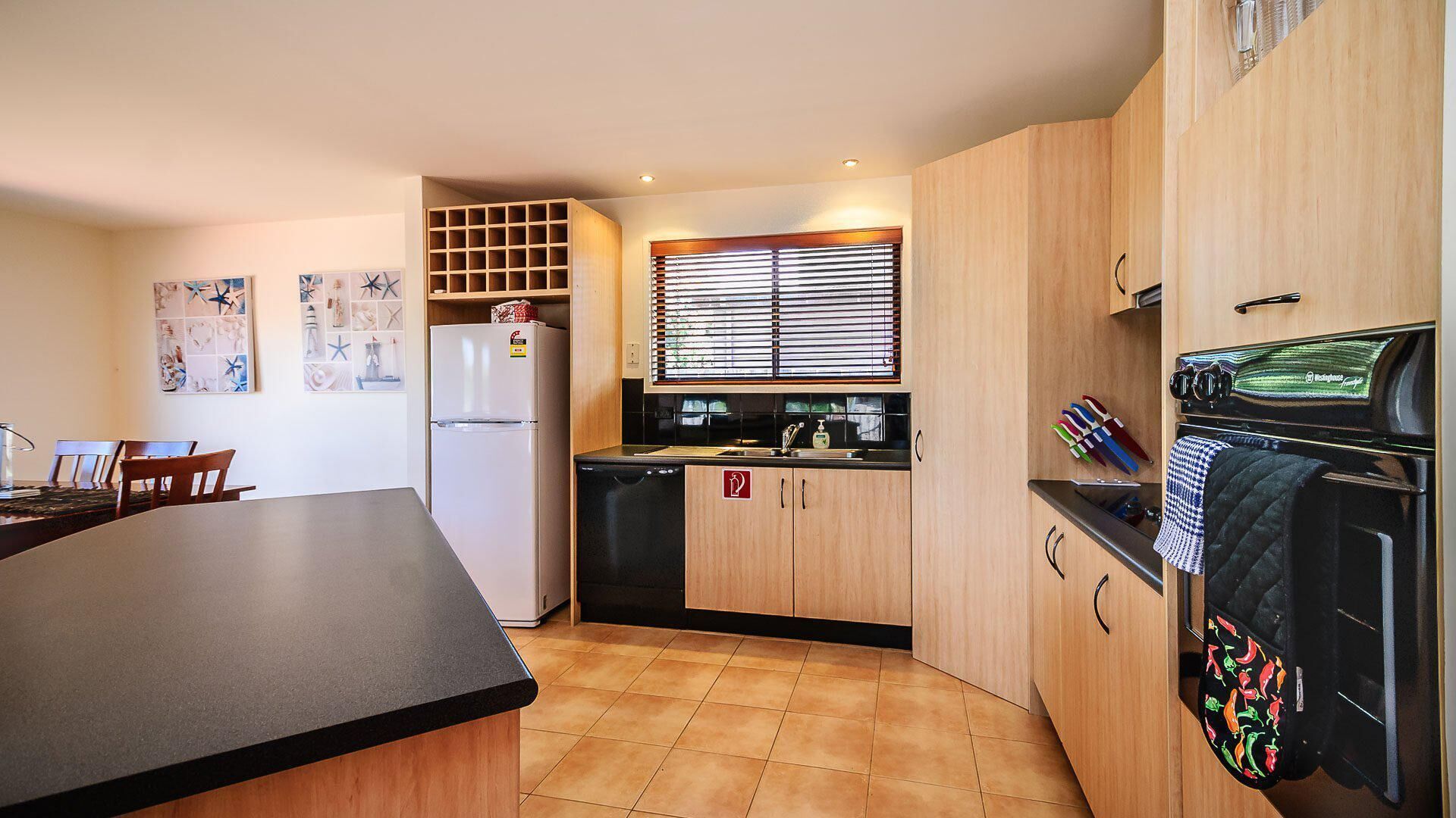 A compact kitchen with a refrigerator, sink, and stove. There is a dining area with chairs and a table.