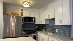 A modern kitchen with white cabinets, a stainless steel refrigerator, a microwave, and a sink.