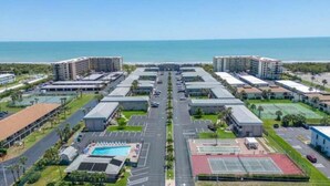 A hotel complex with multiple buildings, a central road, parking areas, and a pool.