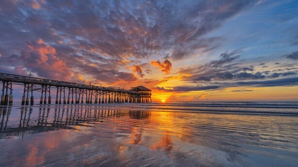 A pier extending into calm waters at sunset with a clear sky above.