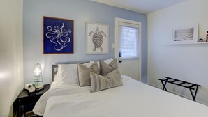 Une chambre à coucher avec un lit, des oreillers, une table de chevet, une horloge murale et des œuvres d’art encadrées.