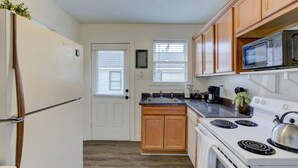 Une cuisine de taille réduite équipée d’un réfrigérateur, d’une cuisinière, d’un four à micro-ondes et de meubles de rangement en bois.