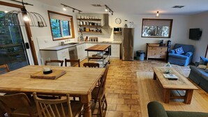 A modern kitchen with white cabinets, a wooden dining table, and a built-in oven. There is a large window providing natural light and a view of the outdoors. - A2 @ Port Willy      (Port Willunga)
