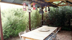 An outdoor wooden table with metal chairs, surrounded by greenery and a brick floor. - A2 @ Port Willy      (Port Willunga)