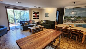 A modern living room with a wooden dining table, sofas, and a large mural of a coastal scene. - A2 @ Port Willy      (Port Willunga)