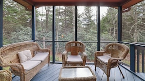 A covered porch with wicker furniture and a glass enclosure, overlooking a forested area. - Private 5BR Escape with Hot Tub & Games, Near Lakes, Hikes & Water Parks (Long Pond)