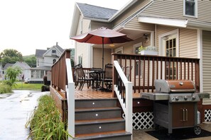 Una terraza de madera con una parrilla, mobiliario exterior y un porche cubierto.