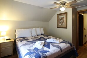 Una cama bien hecha con colcha de estampado de estrellas, un ventilador de techo y una lámpara de noche.