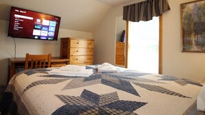 Une chambre d’hôtel avec un grand lit, un téléviseur fixé au mur, une commode en bois et un tableau accroché au mur.