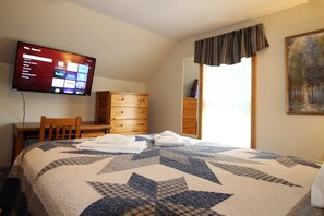 Quarto de hotel com cama grande, televisão na parede, cómoda de madeira e um quadro.