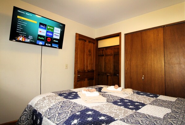 A bedroom with a bed, a TV mounted on the wall displaying a streaming service interface, and two wooden wardrobes. - Cooperstown Baseball Rentals - Championship #3 (Oneonta)