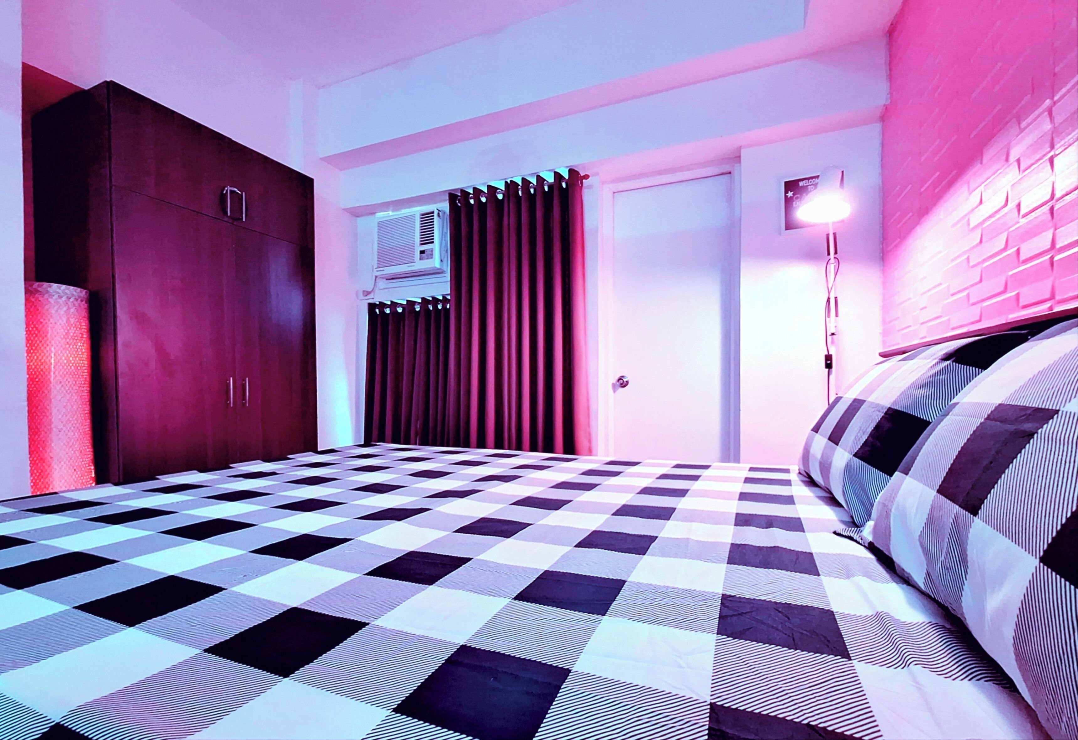 Ein Schlafzimmer mit kariertem Bettbezug, einem Kleiderschrank, einer Tür und einer Wand-Klimaanlage.