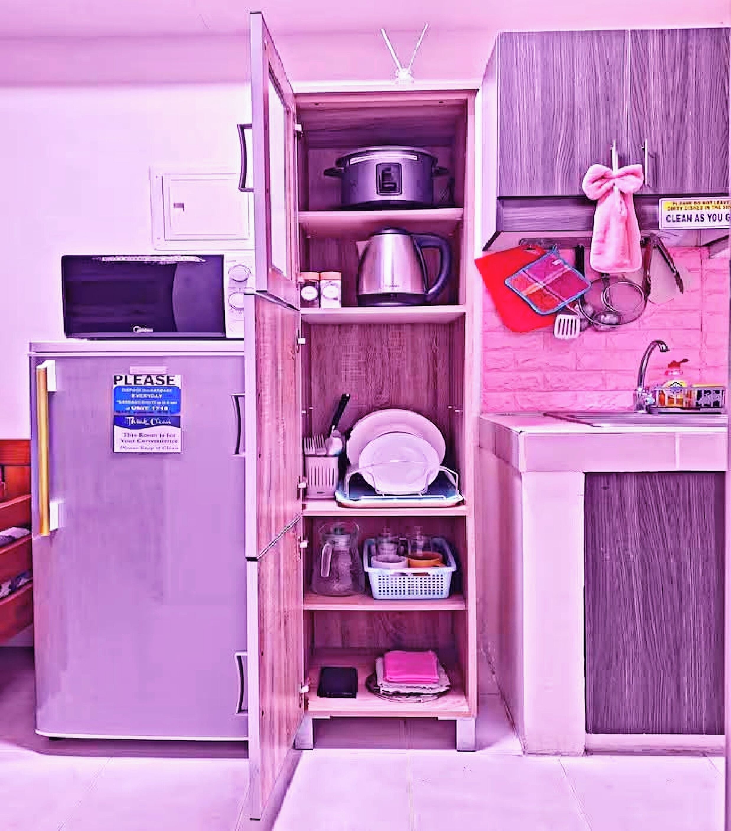 Una cocina compacta con microondas, un refrigerador pequeño y un armario con diferentes utensilios de cocina.
