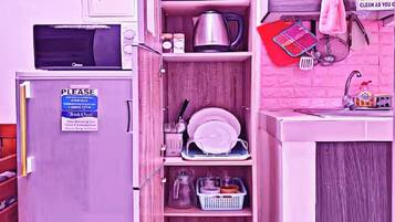 Una cocina compacta con microondas, un refrigerador pequeño y un armario con diferentes utensilios de cocina.