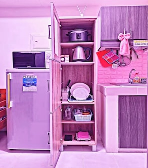 Uma cozinha compacta com micro-ondas, um frigorífico pequeno e um armário com utensílios de cozinha.