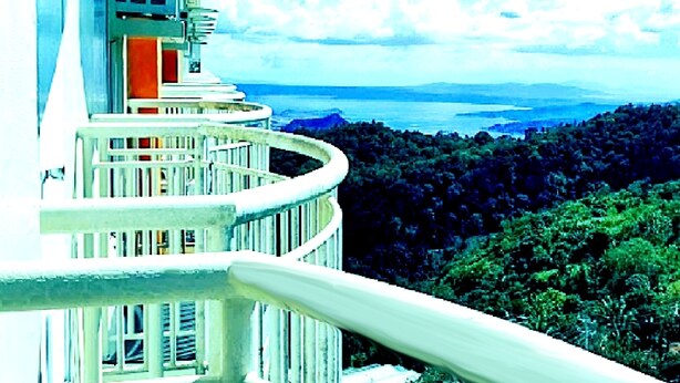 A hotel with a balcony overlooking a forested landscape and a body of water.