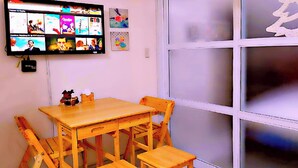 A room with a wooden table and chairs, a flat-screen TV mounted on the wall, and a large window with frosted glass.