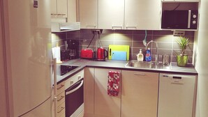 A compact kitchen with white cabinets, a microwave, a coffee maker, and a dishwasher. - The cosmopolitan apartment (Turku)