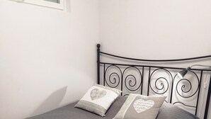 A bed with a metal frame, a quilted grey bedspread, and two pillows with heart designs. - The cosmopolitan apartment (Turku)
