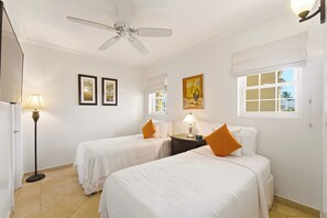 A hotel room with two beds, a ceiling fan, a nightstand with a lamp, and artwork on the walls.