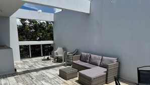 Une terrasse sur le toit avec un canapé d’angle gris, des chaises en osier, une petite table et un barbecue.
