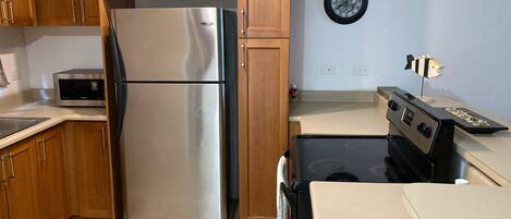 Une cuisine avec des meubles en bois, un réfrigérateur en acier inoxydable, un four à micro-ondes, une cuisinière et une horloge murale.
