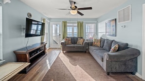 A living room with a ceiling fan, a flat-screen TV, a gray sofa, and a wooden entertainment center.