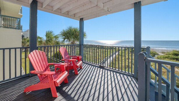 A covered deck with red Adirondack chairs overlooking a beach.