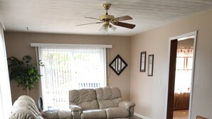 Un salon spacieux doté d’un ventilateur de plafond, de deux canapés en cuir, d’une table basse en bois et d’un plancher en bois franc.