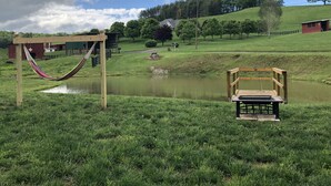Un espace verdoyant avec un hamac, une terrasse en bois et un étang.