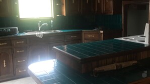 Une cuisine avec des meubles de rangement en bois, un plan de travail recouvert de carreaux verts et une fenêtre qui laisse entrer la lumière naturelle.
