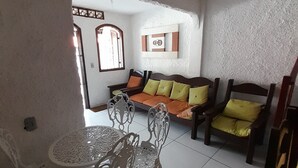 Un coin repas avec une table ronde et des chaises, un canapé avec des coussins et une étagère murale agrémentée d’objets décoratifs.