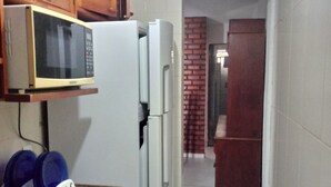Une cuisine avec des meubles en bois, un four à micro-ondes, un réfrigérateur et un évier équipé d’un égouttoir bleu.