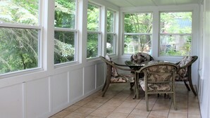 Un patio cubierto con una mesa y sillas, ventanas amplias y vistas a follaje.