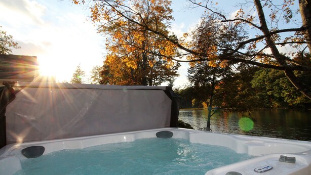 Un jacuzzi con vistas a un lago y árboles otoñales.