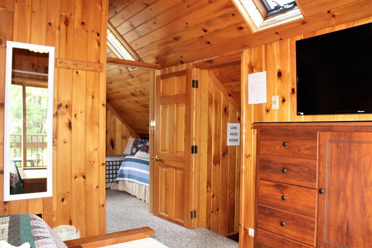 A wooden cabin with a loft bedroom, a low head room sign, and a television on the wall.
