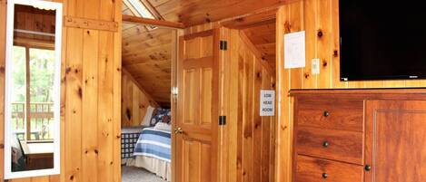 A wooden cabin with a loft bedroom, a low head room sign, and a television on the wall.