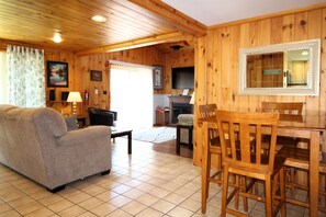 L’intérieur d’un chalet en bois comprend un canapé, une table à manger, des chaises, une cheminée et un coin cuisine.