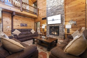 Ein gemütliches Blockhaus-Interieur mit Kamin aus Stein, Holzwänden und einem Balkon.