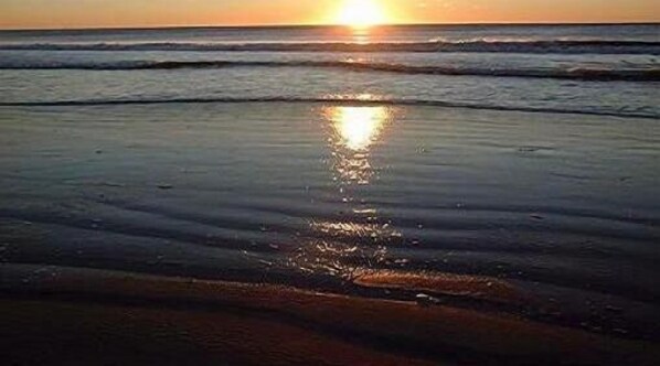 Een strand bij zonsondergang met golven en een zonnespiegeling in het natte zand.