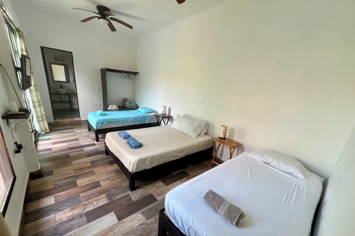 A hotel room with two beds, a ceiling fan, a bedside table with a lamp, and a wooden floor.