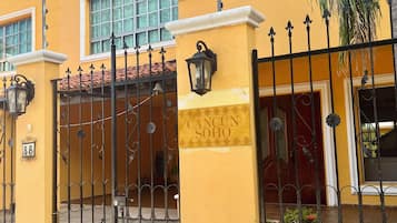 Un edificio amarillo con una entrada protegida por una reja, un letrero que dice